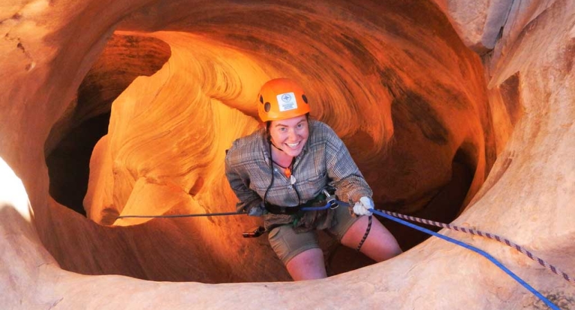 A person wearing safety gear is attached to ropes as they rappel into a red canyon. 